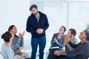 Beginnings-Treatment-Centers-rehab-group-applauding-delighted-man-standing-up-at-therapy-session