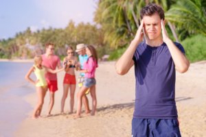 beginningstreatment-5-tips-for-stopping-cravings-article-photo-stress-and-headache-young-man-feeling-bad-while-his-friend-enjoying-beach-party-519460792