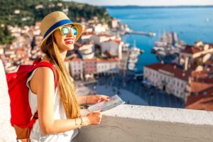 beginningstreatment-7-tips-for-staying-sober-while-traveling-article-photo-young-female-traveler-with-red-backpack-and-hat-enjoying-the-view-from-george-s-tower-on-piran-old-459099973