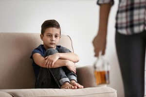 beginningstreatment-7-common-characteristics-of-adult-children-of-alcoholics-article-photo-sad-little-boy-and-blurred-woman-with-bottle-of-alcohol-indoors-793067572