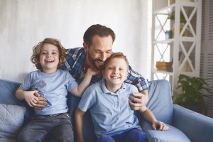 A father hugs his two sons, one with each arm, as they all laugh happily together