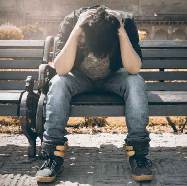 Anxious man holding his head down while sitting on a park bench