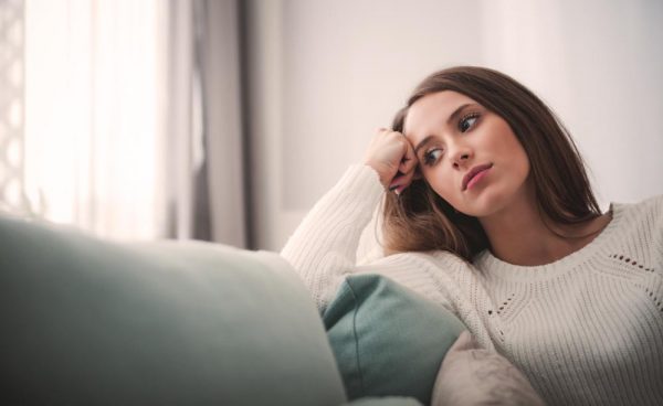 Sad woman sitting on a couch looking out the window